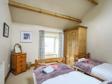 A bedroom with two single beds a wooden wardrobe a chest of drawers and a window with curtains at Fron Fawr in Nefyn