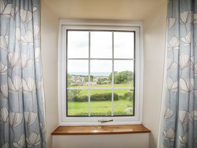 A window with curtains showing a view of green fields trees and houses at Fron Fawr in Nefyn