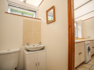 A small bathroom with a toilet and sink next to a kitchen with cabinets and a washing machine at Fron Fawr in Nefyn