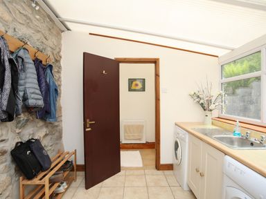 A utility room with a washing machine, dryer, sink, coat rack with jackets, shoe rack, and a door leading to another room at Fron Fawr in Nefyn
