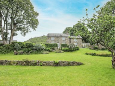 A stone house with a grassy garden and outdoor furniture surrounded by trees at Fron Fawr in Nefyn
