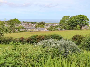 A green garden with shrubs and trees overlooking a village and the sea at Fron Fawr in Nefyn