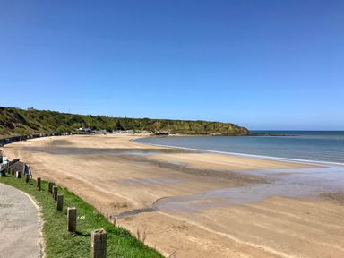 A sandy beach with a curved shoreline and grassy hill in the background at Fron Fawr in Nefyn