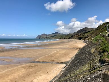 A sandy beach with waves and grassy hills under a blue sky at Fron Fawr in Nefyn