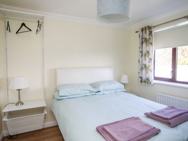 A bedroom with a double bed two bedside lamps and a window with floral curtains at The Gables in Trearddur Bay