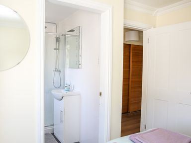 A bathroom with a shower and sink visible through an open door in a bedroom at The Gables in Trearddur Bay