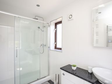 A bathroom with a glass shower enclosure a small window and a countertop with a sink and a small plant at The Gables in Trearddur Bay
