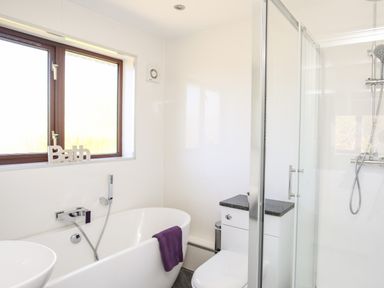 A bathroom with a bathtub, shower enclosure, toilet, and a window at The Gables in Trearddur Bay