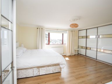 A bedroom with a bed beside a window and large sliding wardrobe at The Gables in Trearddur Bay