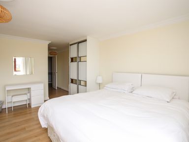 A bedroom with a large bed a white desk with a stool a mirror and a wardrobe at The Gables in Trearddur Bay