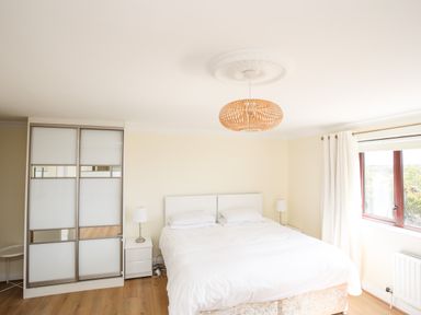 A bedroom with a double bed two bedside tables with lamps a wardrobe and a window with white curtains at The Gables in Trearddur Bay