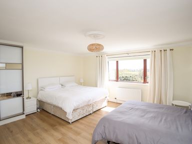 A bedroom with two beds bedside tables lamps curtains and a large window at The Gables in Trearddur Bay