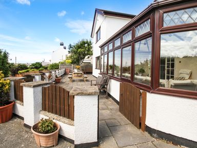 A patio area with wooden gates and a picnic table outside a white house with large windows at The Gables in Trearddur Bay