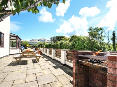 An outdoor patio area with a brick barbecue grill a wooden picnic table and potted plants surrounded by greenery