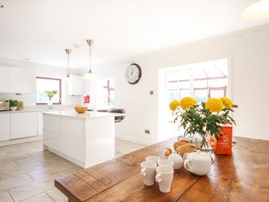 A kitchen with a wooden table set with cups a teapot toast flowers and cereal at The Gables in Trearddur Bay