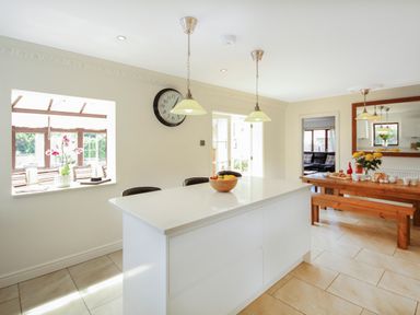 A kitchen with a white island and a wooden dining table with bench seating at The Gables in Trearddur Bay