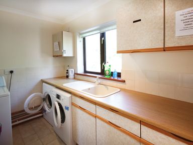 A utility room with washing machines a sink cleaning products and cabinets at The Gables in Trearddur Bay