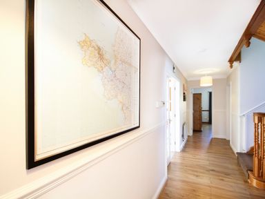 A hallway with a large framed map on the wall wooden floor and a staircase at The Gables in Trearddur Bay