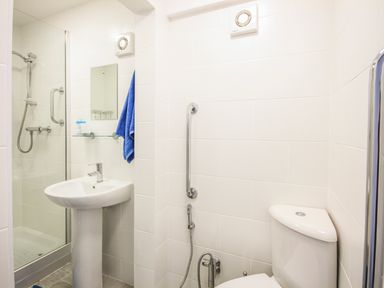 A bathroom with a shower, pedestal sink, toilet, towel, and grab bars at The Gables in Trearddur Bay