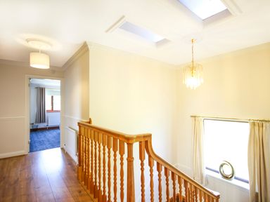 A hallway with wooden railing and hardwood floor leading to a room with carpet at The Gables in Trearddur Bay