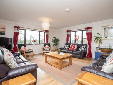 A living room with leather sofas wooden coffee table red curtains and plants at The Gables in Trearddur Bay
