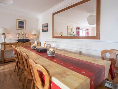 A dining room with a wooden table covered with a red and beige tablecloth and wooden chairs at The Gables in Trearddur Bay