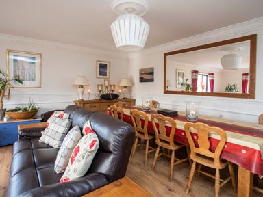 A dining room with a wooden table and chairs and a leather sofa with cushions at The Gables in Trearddur Bay