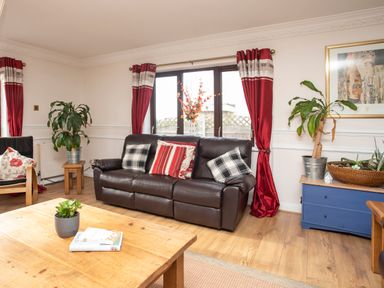 A living room with a leather sofa and red curtains at The Gables in Trearddur Bay