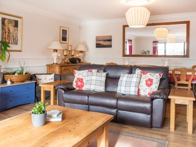 A living room with a brown leather sofa and wooden tables at The Gables in Trearddur Bay