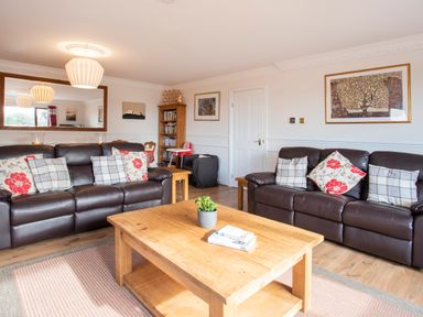 A living room with two brown leather sofas a wooden coffee table with books and a plant a bookshelf and wall art at The Gables in Trearddur Bay