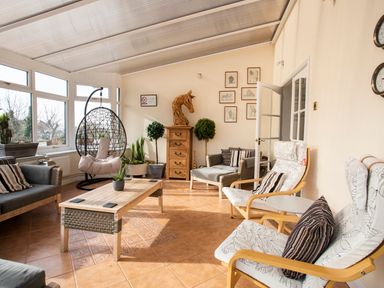 A sunroom with wicker and wooden chairs a hanging wicker egg chair wooden chest of drawers and potted plants at The Gables in Trearddur Bay