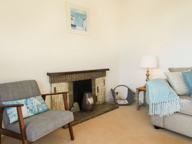 A living room with a gray armchair a fireplace a side table with a lamp and a beige sofa with cushions and a blanket at Garnedd Lwyd in Llanfair