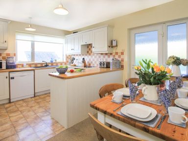 A kitchen and dining area with a wooden table set with dishes and flowers at Garnedd Lwyd in Llanfair