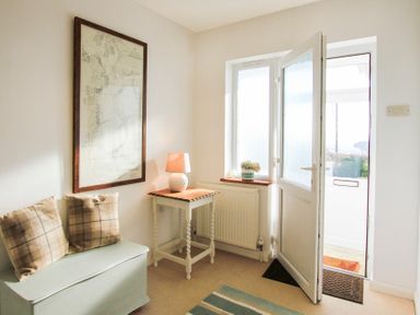 An entryway with a bench and two plaid cushions a side table with a lamp a framed map on the wall and an open door at Garnedd Lwyd in Llanfair