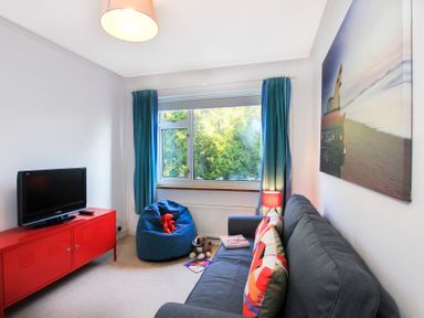 A living room with a gray sofa and colorful pillows a redTV stand and blue bean bag at Garnedd Lwyd in Llanfair