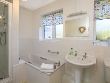 A bathroom with a bathtub shower sink and two windows with patterned blinds at Garnedd Lwyd in Llanfair