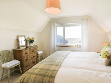 A bedroom with a bed pillows window wooden dresser mirror and two chairs with towels at Garnedd Lwyd in Llanfair