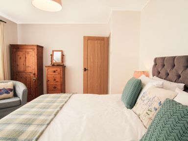 A bedroom with a bed with pillows a wooden wardrobe a chest of drawers with a mirror and an armchair at Garnedd Lwyd in Llanfair