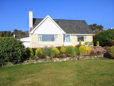 A house with a sloped roof surrounded by shrubs and a grass lawn at Garnedd Lwyd in Llanfair