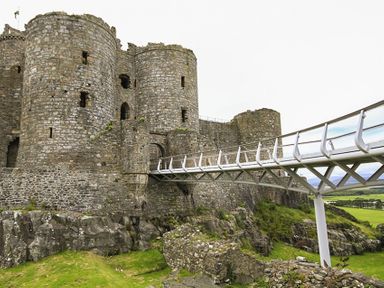 A stone castle with a modern metal bridge over rocky terrain at Garnedd Lwyd in Llanfair