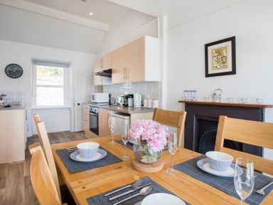A kitchen with wooden dining table set for four with pink flowers and light wood cabinets at Glan Dwr Bach in Glyn Garth