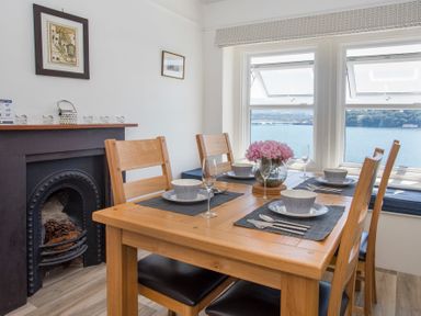 A dining area with a wooden table set for four near windows with a water view at Glan Dwr Bach in Glyn Garth