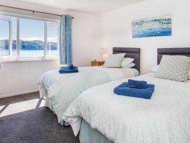 A bedroom with two single beds blue towels and a window with a water view at Glan Dwr Bach in Glyn Garth