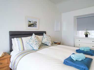 A bedroom with a bed with pillows and folded towels next to a window with a blind at Glan Dwr Bach in Glyn Garth