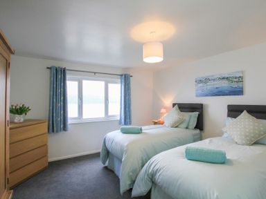 A bedroom with two single beds a wooden wardrobe and chest of drawers with a window and blue curtains at Glan Dwr Bach in Glyn Garth