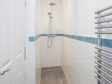 A shower area with a rain showerhead and handheld shower in a tiled bathroom at Glan Dwr Bach in Glyn Garth