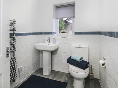 A bathroom with a pedestal sink toilet and window with towel on toilet at Glan Dwr Bach in Glyn Garth