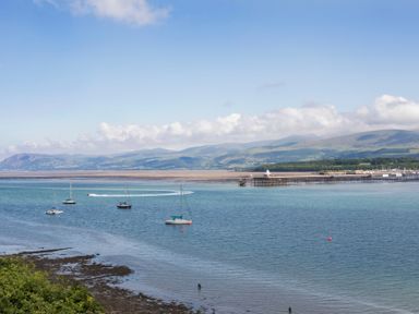 A coastal view with boats on the water and a pier with hills in the background at Glan Dwr Bach in Glyn Garth