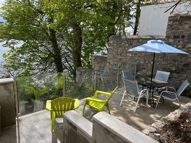 An outdoor patio area with green chairs and a table with chairs and an umbrella at Glan Dwr Bach in Glyn Garth