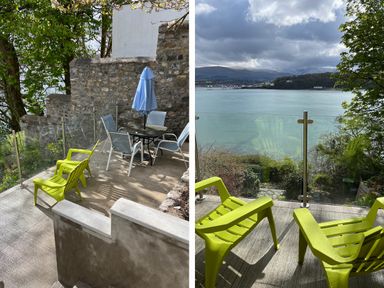 An outdoor terrace with yellow chairs and a table with blue umbrella overlooking a body of water and hills at Glan Dwr Bach in Glyn Garth